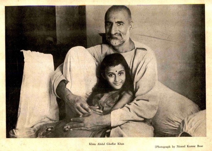 Printed archival plate: Khan Abdul Ghaffar Khan reclining against bolsters with a young girl seated in front of him, both looking at the camera. The printed caption below reads 'Khan Abdul Ghaffar Khan — Photograph by Nirmal Kumar Bose'.