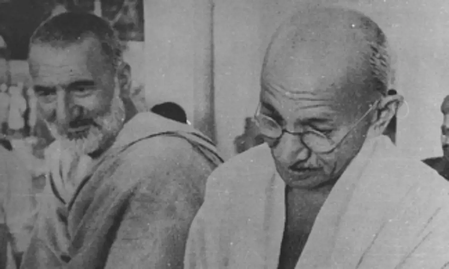 Grainy black and white photograph: Khan Abdul Ghaffar Khan on the left in a shawl, listening; Mahatma Gandhi on the right, head lowered, in a white shawl and round spectacles.